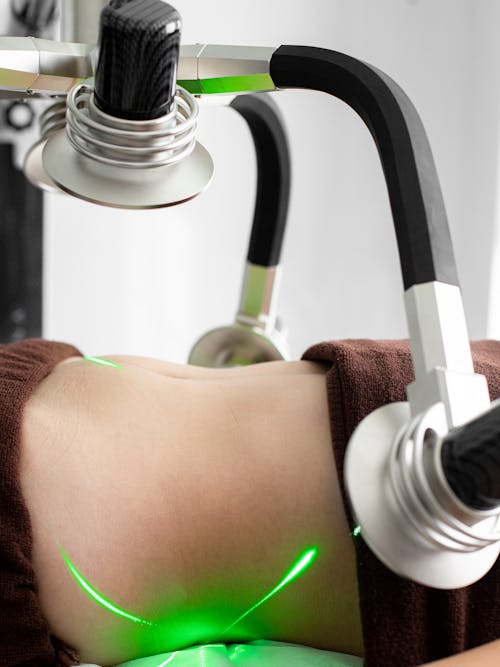 Crop faceless female client lying under modern laser weight loss machine with heads during treatment in modern light medical clinic