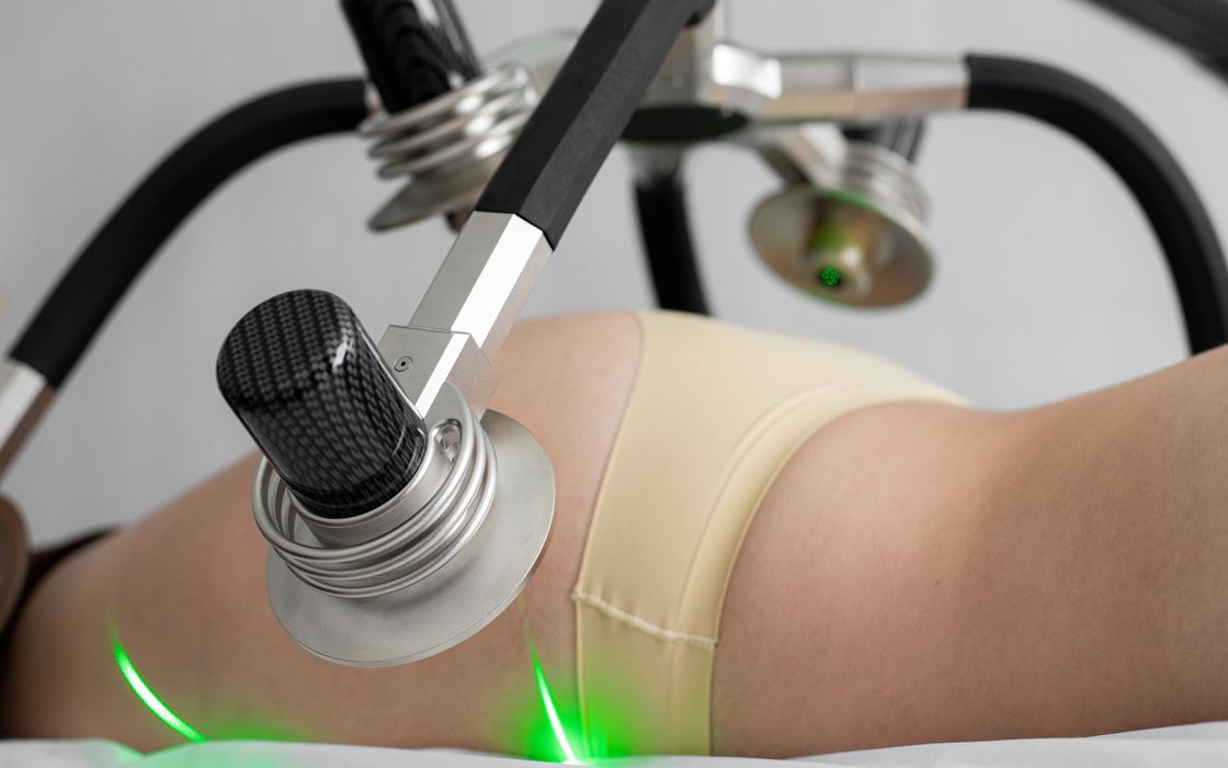 Side view of crop anonymous female in underwear lying and doing non invasive laser body treatment against light wall in