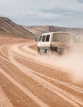 Vehicle driving on sandy dry terrain in desert near mountains under cloudy sky in daylight