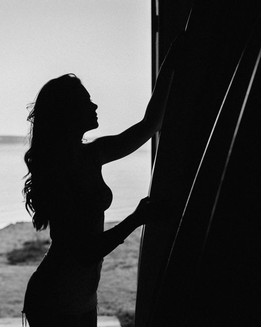 Black and white side view silhouette of unrecognizable slim female standing near wall against calm sea in summer