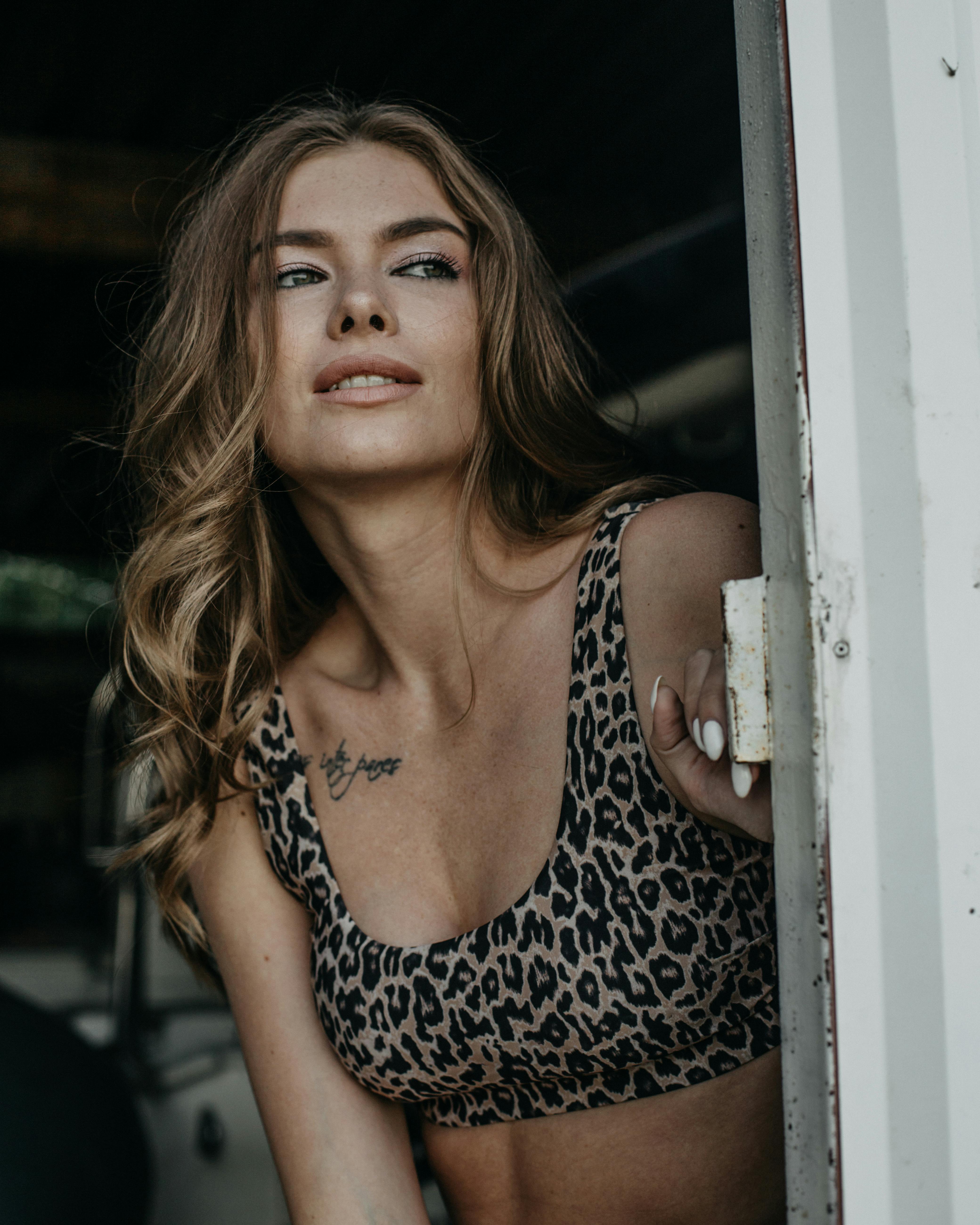 Charming young female with wavy hair in stylish clothes standing near entrance of house and looking away