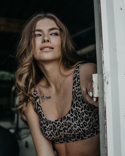 Charming young female with wavy hair in stylish clothes standing near entrance of house and looking away