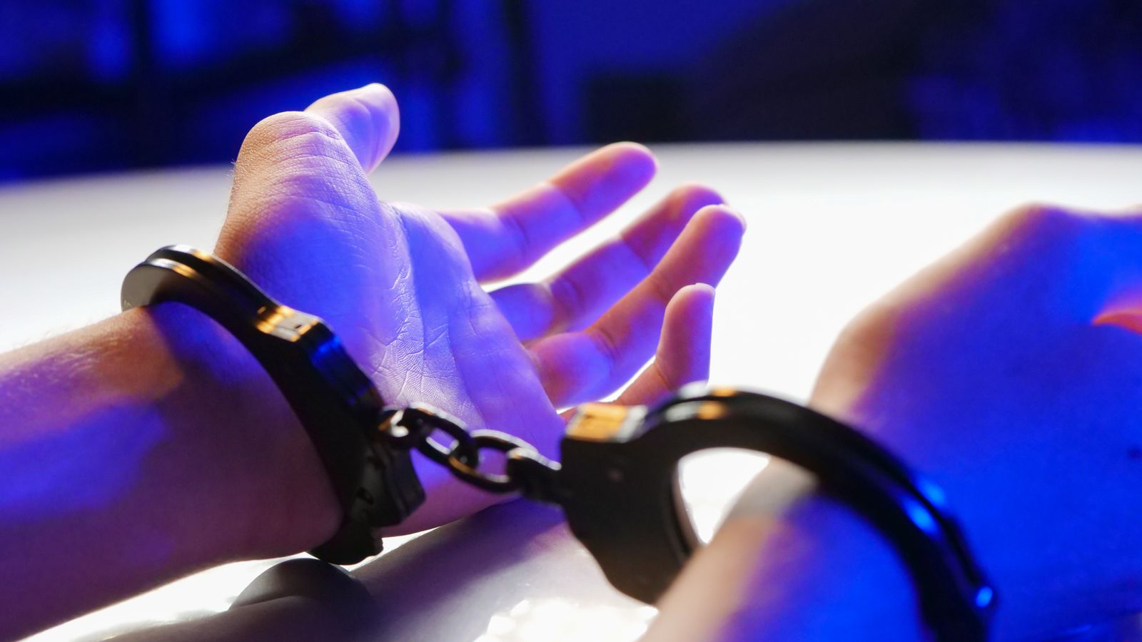 A close-up image of handcuffed hands under blue lighting, symbolizing law enforcement.