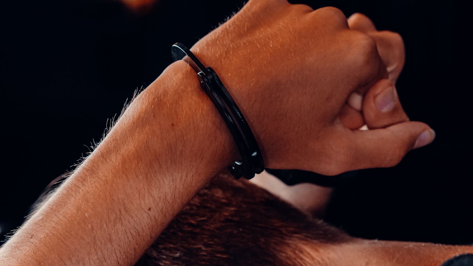 A close-up of a hand in handcuffs against a dark background, depicting a concept of security and restraint.