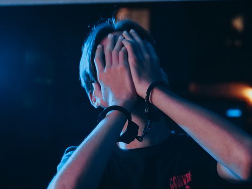 Free A person in handcuffs conceals their face under a blue light, suggesting a crime scene. Stock Photo