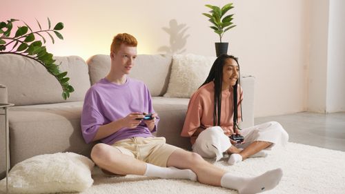 Free A young man and woman playing video games together on a cozy living room floor. Stock Photo