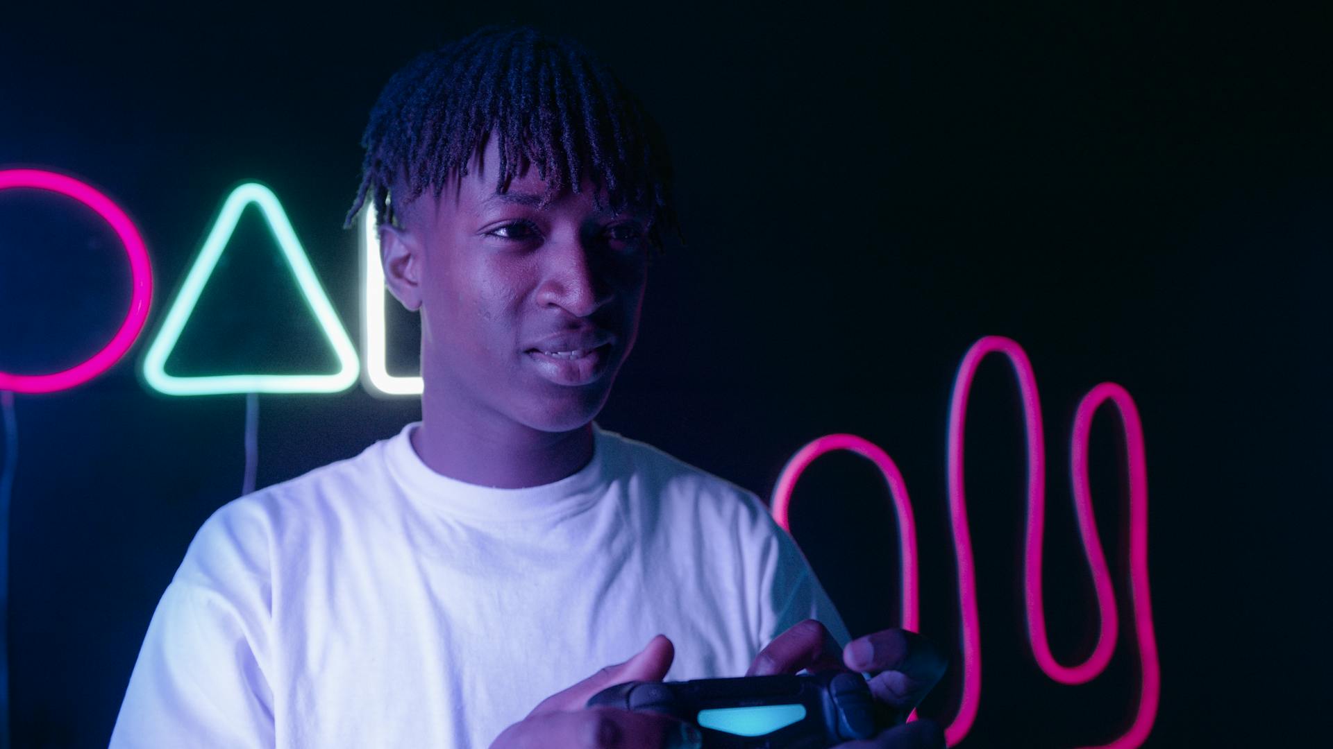 A young man holding a game controller, surrounded by vibrant neon lights in a dark setting.