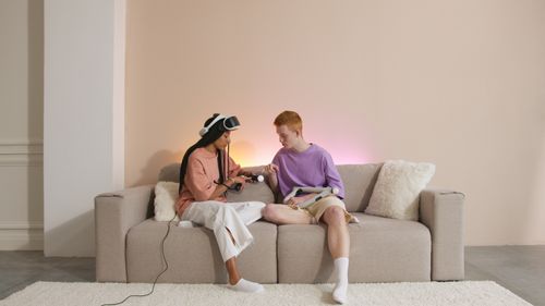 Free A diverse couple sitting on a sofa, playing with VR controllers indoors. Stock Photo
