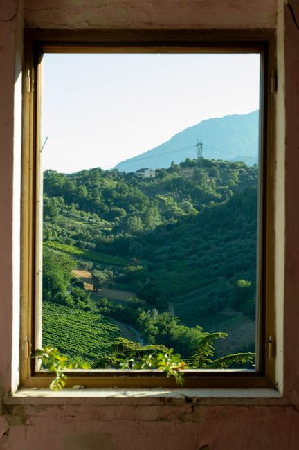 A tranquil view of a verdant valley and distant hills framed by a window, showcasing nature's beauty.