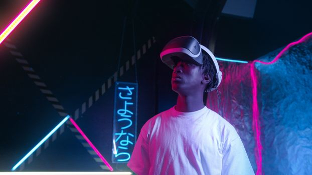 A young man using virtual reality glasses in a neon-lit environment, showcasing technology and innovation.
