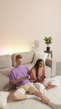 Young couple sitting on carpet in bright room, sharing fun gaming time with controllers.