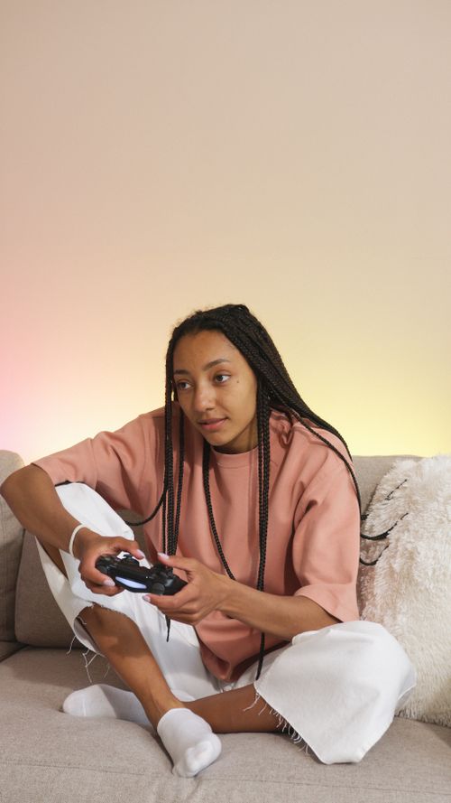 Free A young woman with braided hair enjoying a video game session on the couch. Stock Photo