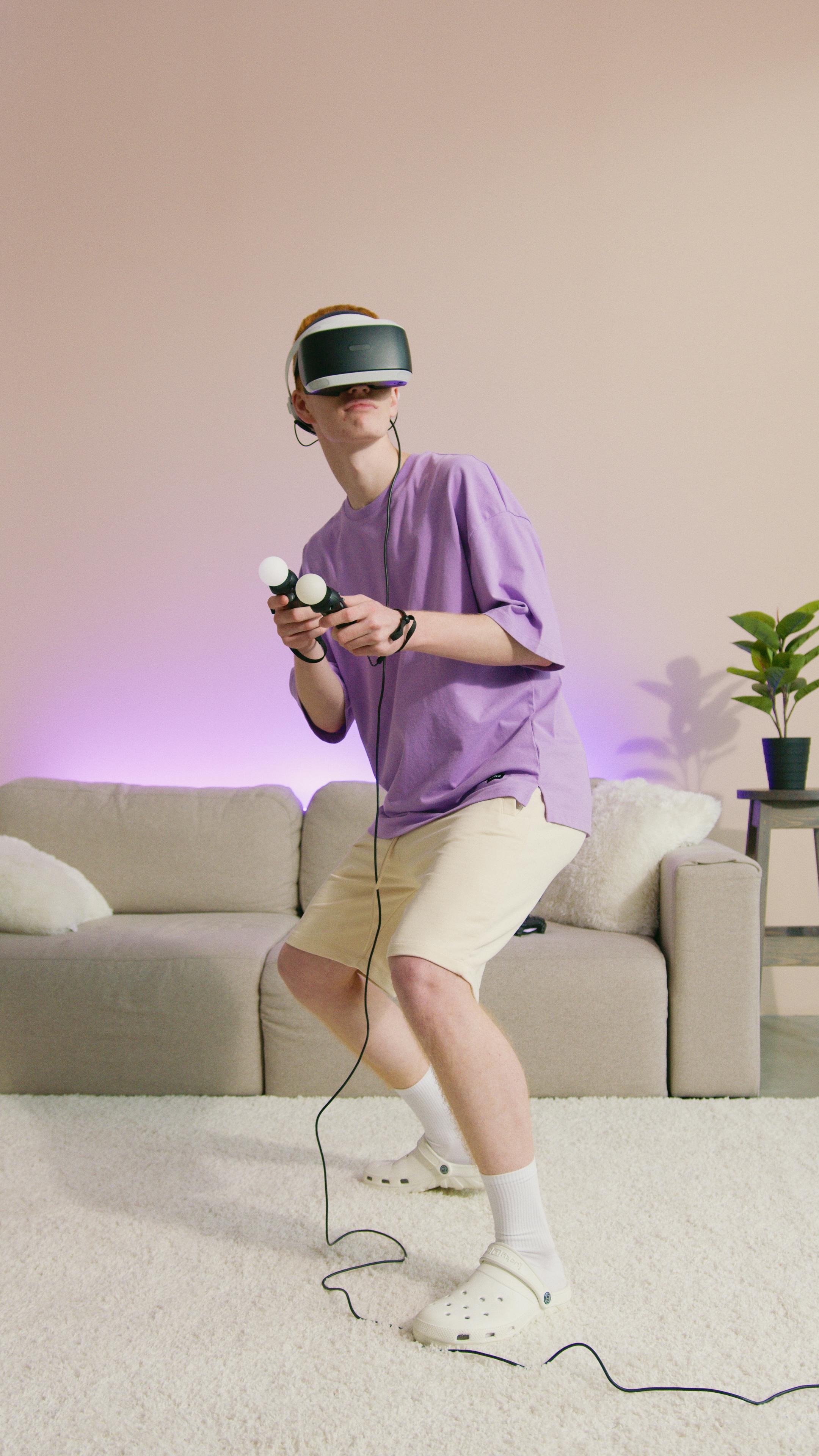 a person in purple shirt wearing vr goggles holding game controllers