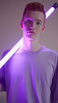 Portrait of a young man indoors with a glowing LED stick casting a purple hue.