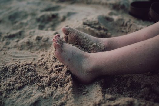 Crop anonymous barefoot child digging loose sand in sunny day on blurred background