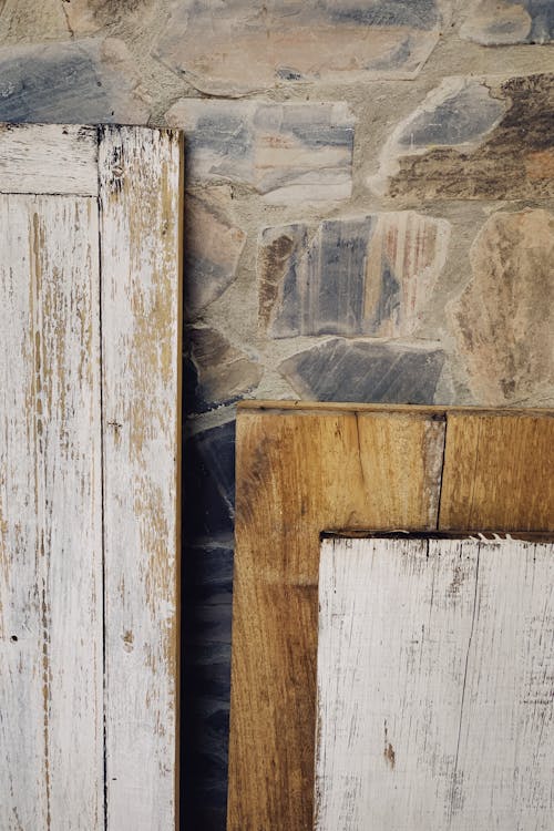 Tops parts of shabby wooden planks with white paint leaning against old multicolored stone wall