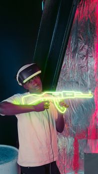 A young man immerses in virtual reality, holding a neon gun, in a tech-inspired room filled with vibrant colors.