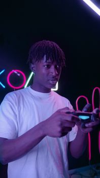 A young man with braided hair intensely plays video games in a neon-lit room.