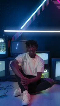 A young man sits in a neon-lit room surrounded by vintage TVs, creating a retro tech vibe.