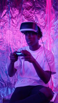 Young man wearing VR headset and gaming with intense neon backdrop, fully immersed in virtual reality.