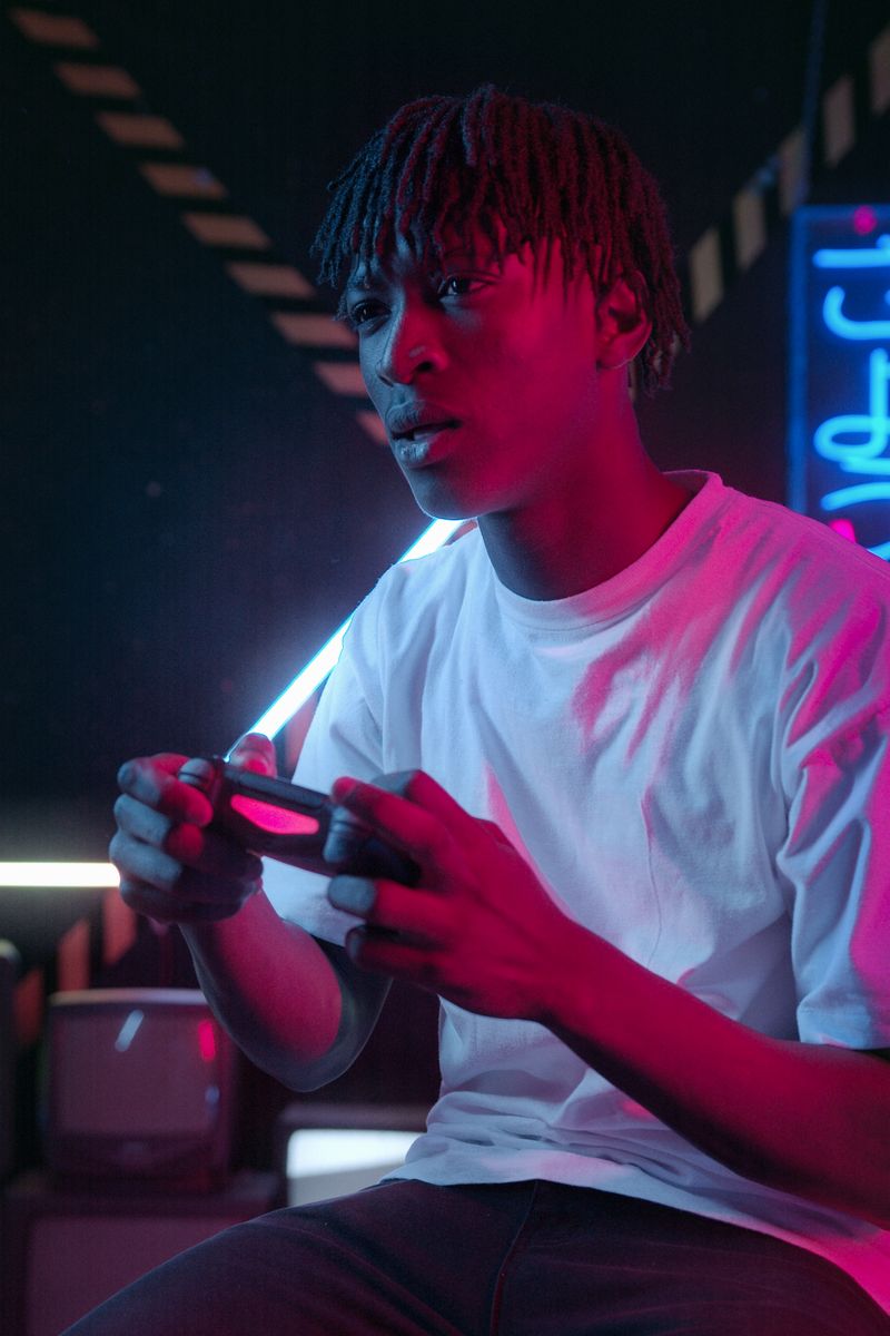 A young man plays video games with a controller in a neon-lit room, showcasing modern gaming culture.