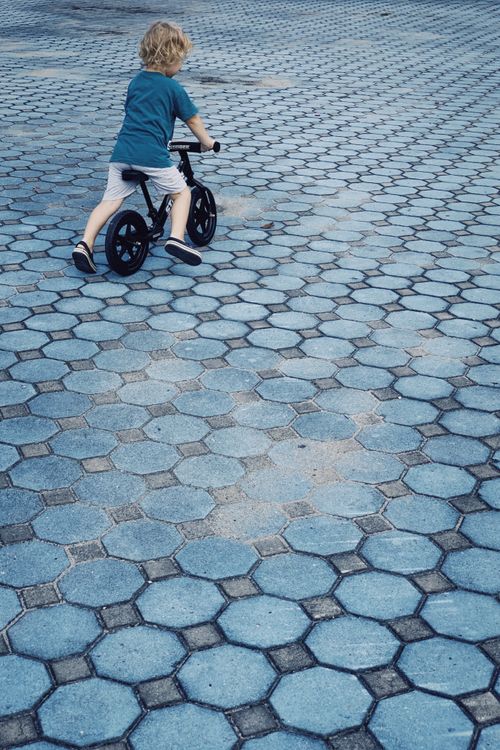 Free From above back view of little blond kid riding bicycle on pavement in daytime Stock Photo
