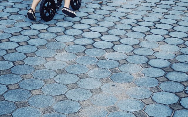 A toddler scooting across hexagon paving on a black Strider balance bike