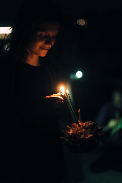 Free Content female looking down while holding krathong and burning candle at dark night Stock Photo
