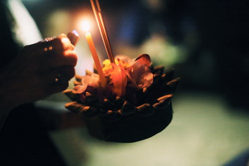 Foto gratuita de una persona anónima quemando una vela en un krathong en la oscuridad sobre un fondo borroso