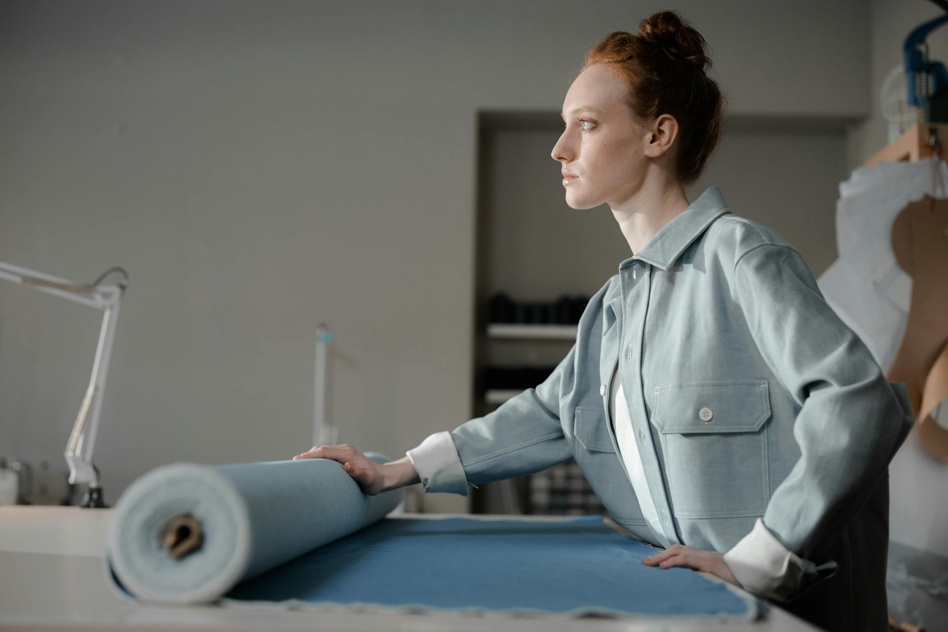 A female fashion designer positioned side view, holding a roll of blue fabric in a studio setting, showcasing creativity.