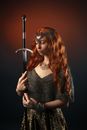 Concentrated young female with ginger long hair with necklace and wearing chainmail armor and costume of warrior with sword standing with closed eyes