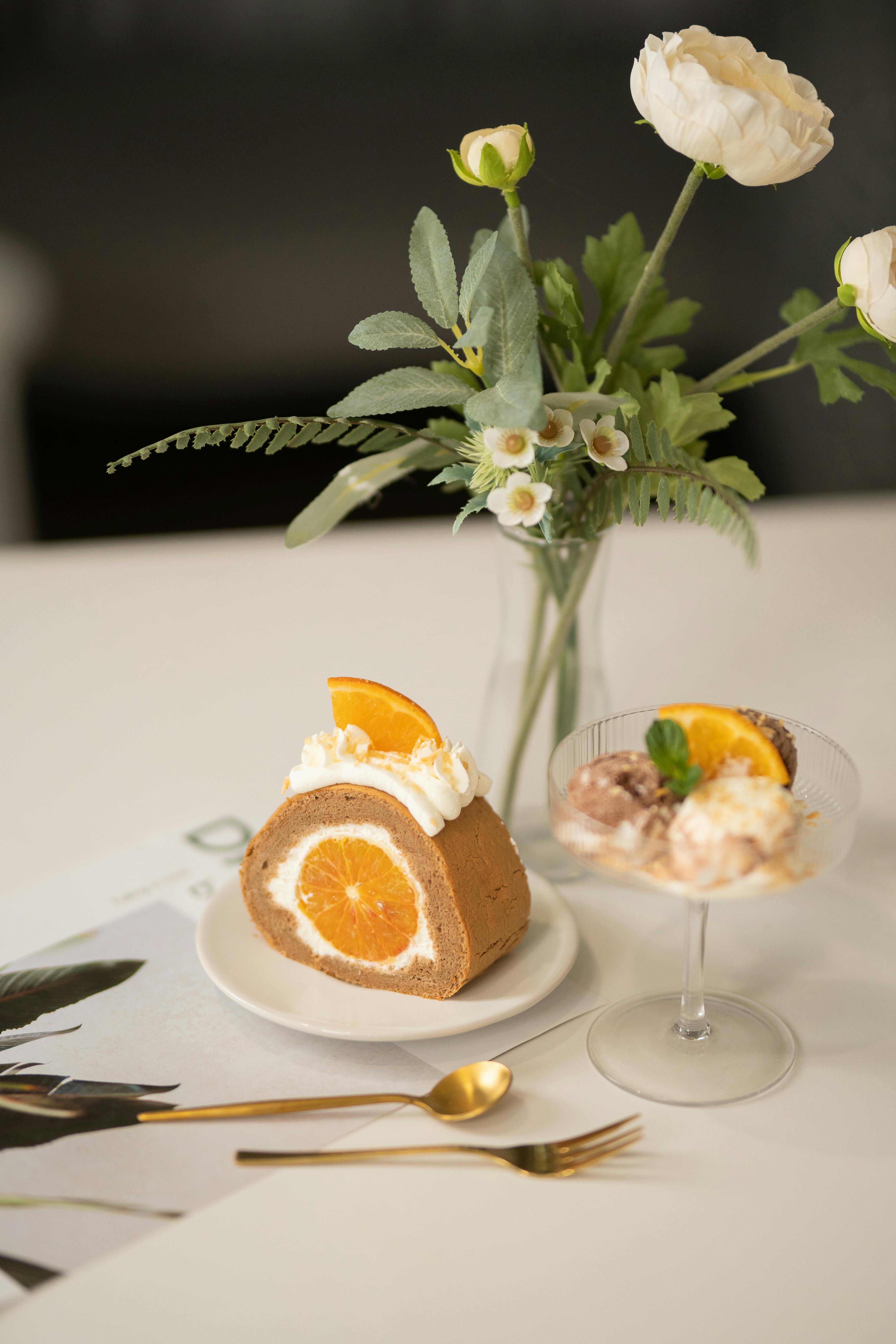 Orange Filled Pastry and Ice Cream Served Next to Vase of White Flowers