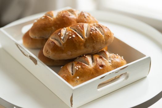 Close-up of artisan bread rolls in a rustic tray, perfectly arranged on a white table, showcasing a homely and delicious treat.