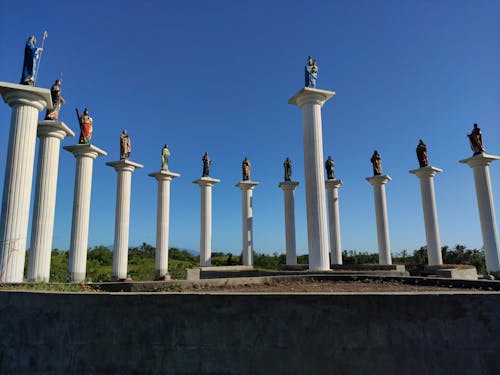 Statues on White Concrete Pillars Under Blue Sky