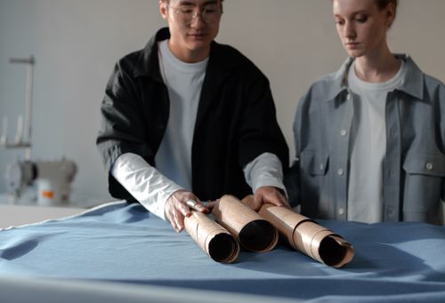 Free Two fashion designers collaborate in a studio on a sewing project, focused on fabric rolls. Stock Photo
