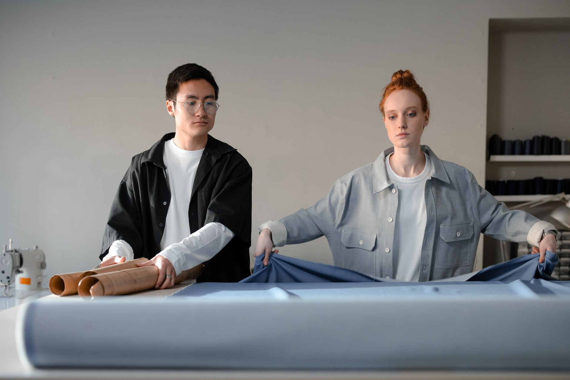 Two tailors collaborating in a fashion studio, working with fabric rolls and materials.