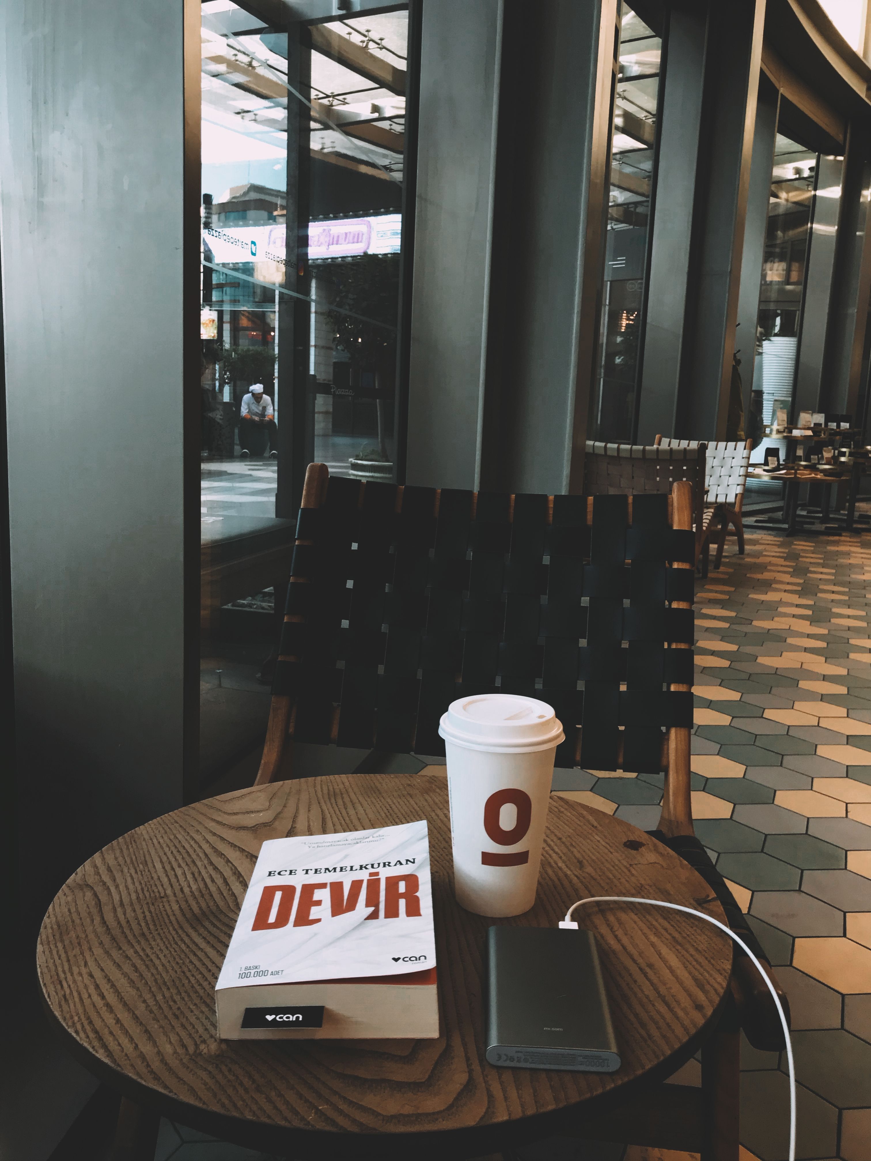 Portable charger with wire placed on wooden round table with book and paper cup with hot coffee in modern cafe