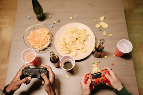 Free Two gamers playing video games with snacks and drinks on table, a perfect setup for gaming night. Stock Photo