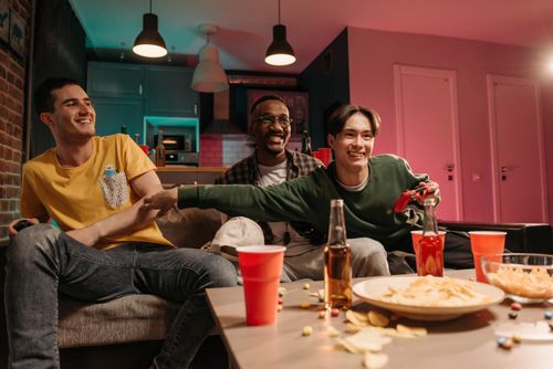 Free Three friends happily engaging in video games with snacks and drinks in a cozy home setting. Stock Photo