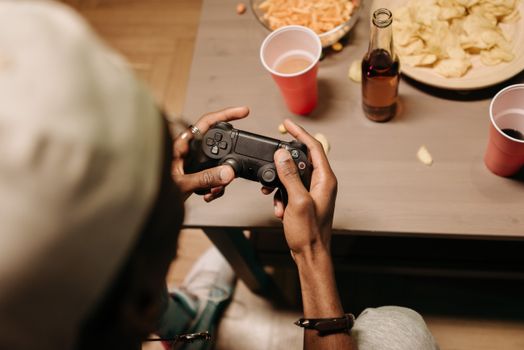 A person enjoying gaming with snacks and drinks on a wooden table, overhead view.