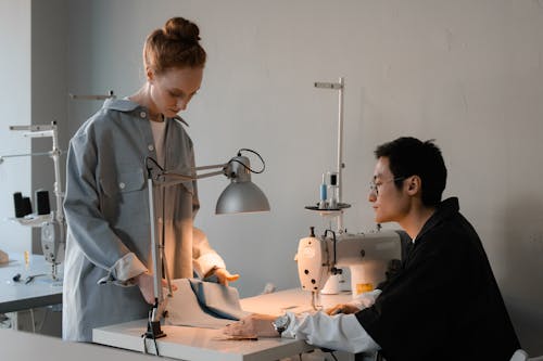 A Woman Standing Across a Man Sitting at a Sewing Machine 