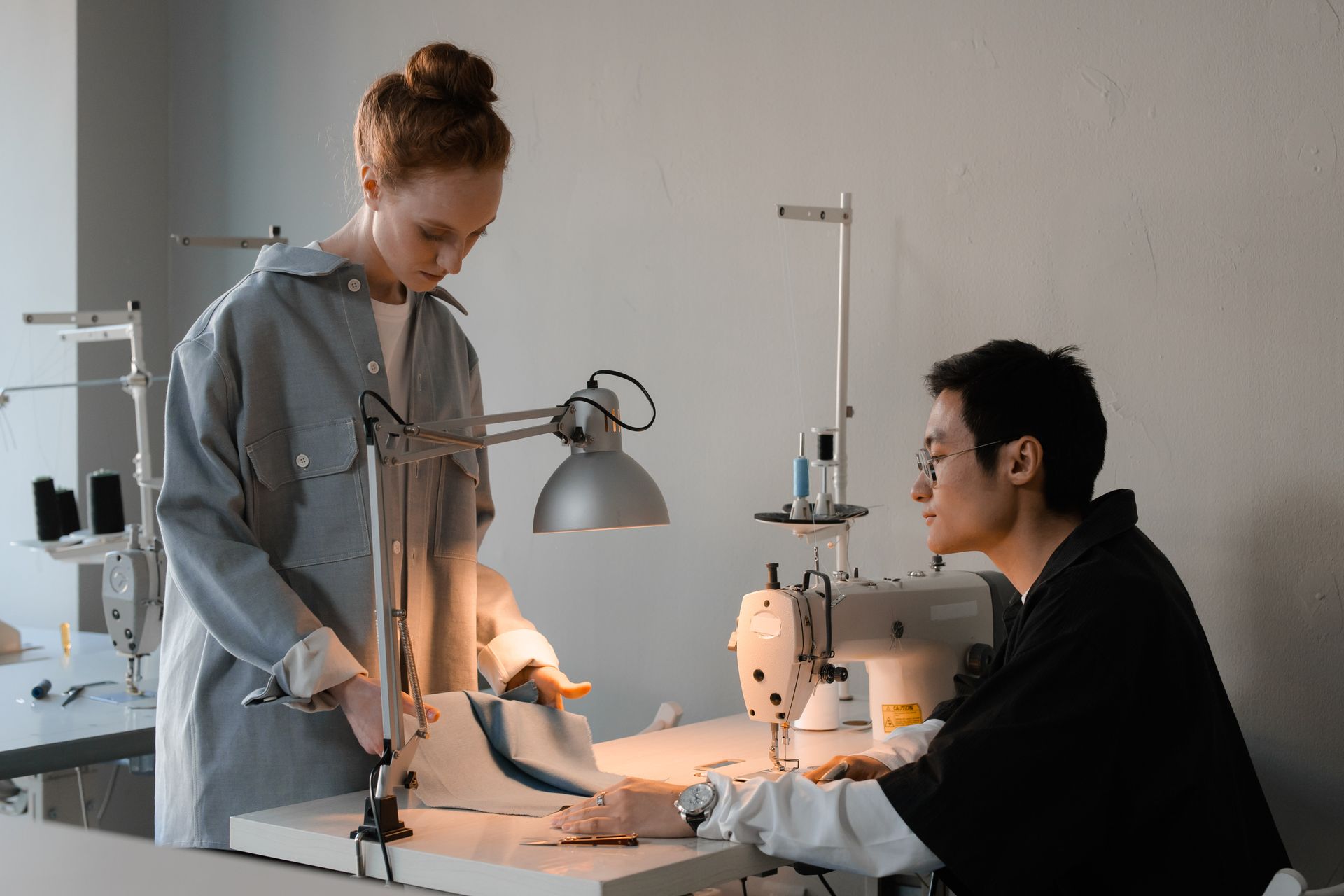 Two tailors work together on fabric design, discussing details under studio lighting.