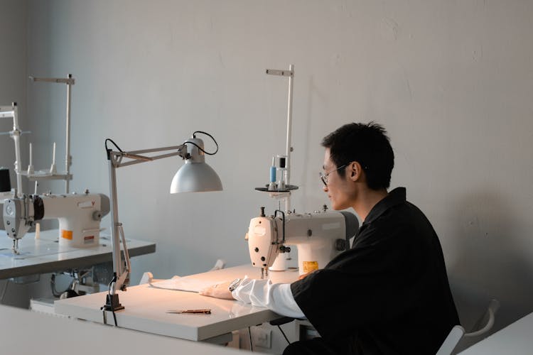 Man In Black Shirt Sitting At Table With Sewing Machine