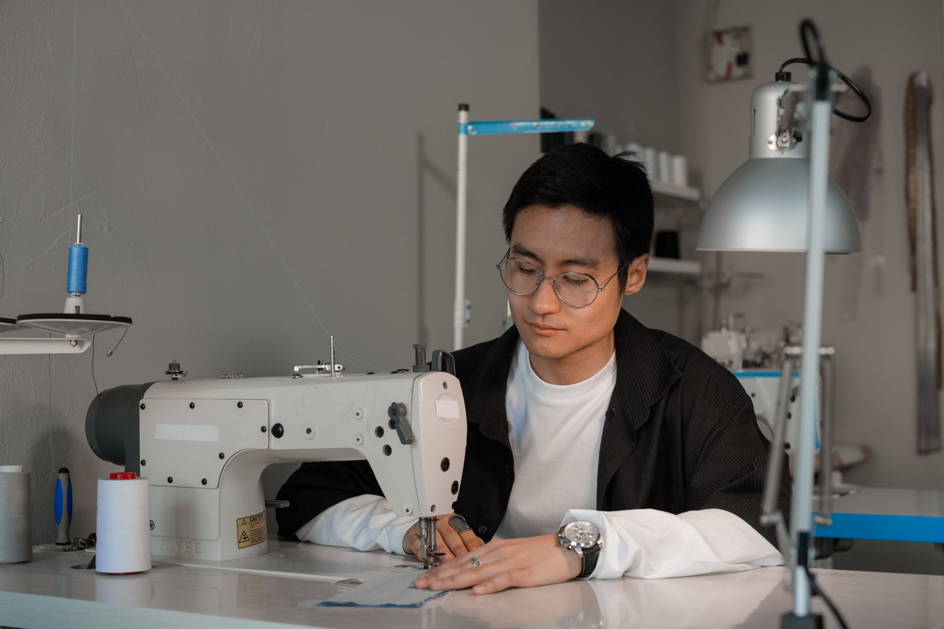Asian man skillfully uses sewing machine indoors, showcasing traditional tailoring craft.