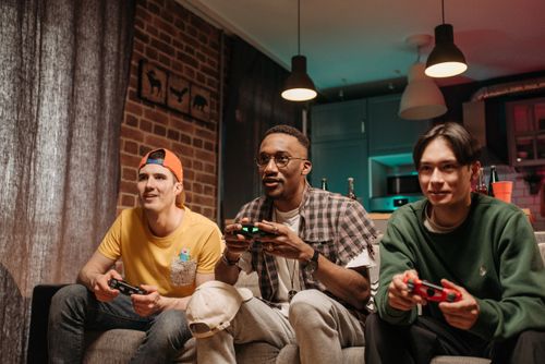 Free Three friends enjoy a fun gaming session together on a cozy sofa, focused and smiling. Stock Photo