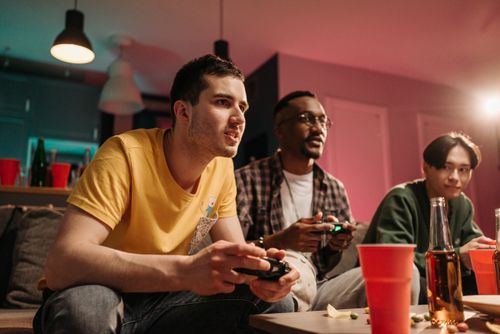Free Diverse group of young adults playing video games on a cozy sofa with refreshments. Stock Photo