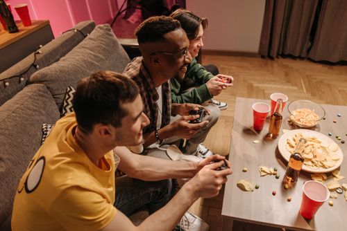 Free Group of friends playing video games and enjoying snacks indoors. Stock Photo
