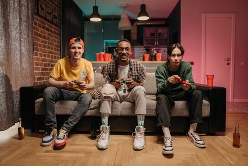 Free Three friends enjoying a gaming session at home, capturing the joy of shared entertainment. Stock Photo