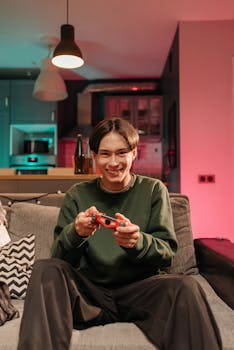 A young man happily playing video games on a couch in a cozy and colorful living room.