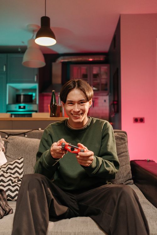 Free A young man happily playing video games on a couch in a cozy and colorful living room. Stock Photo